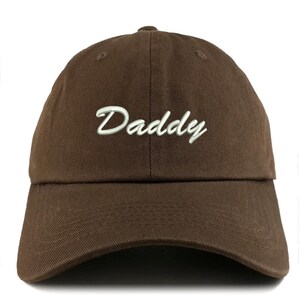 May include: A brown baseball cap with the word "Daddy" embroidered in white script across the front. The cap has a curved brim and a six-panel design.