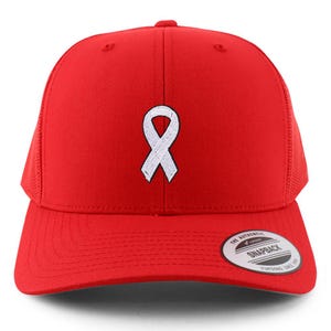 May include: A red trucker hat with a white ribbon embroidered on the front. The hat has a mesh back and a curved brim. The hat also has a snapback closure and a small tag on the brim that says "The Authentic Snapback".
