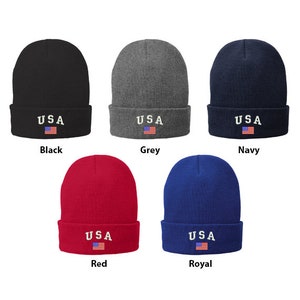 Könnte beinhalten: Fünf Strickmützen in verschiedenen Farben, jede mit einem weißen "USA" bestickt auf der Vorderseite und einer kleinen amerikanischen Flagge darunter gestickt. Die Farben sind Schwarz, Grau, Marine, Rot und Königsblau.
