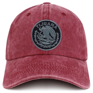May include: A red baseball cap with a curved brim. The cap features a circular patch with the word "TIJUANA" and an emblem of an eagle with a snake. The cap is made of a soft, worn material.