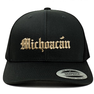 以下が含まれることがあります： 黒いトラッカーハットに、金色の刺繍で「Michoacán」と書いてあります。ハットはメッシュの黒いバックと黒いスナップクロージャーが付いています。
