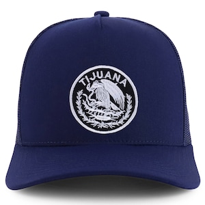 May include: A navy blue trucker hat with a white embroidered patch featuring the text "TIJUANA" and a stylized eagle design.