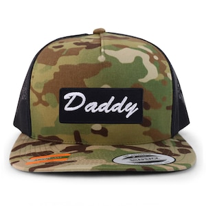 May include: A camouflage trucker hat with a black patch that says "Daddy" in white cursive lettering.