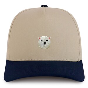May include: A beige and navy blue baseball cap with an embroidered white polar bear face on the front.