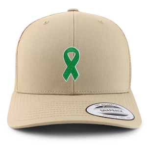 May include: A tan trucker cap featuring a green ribbon emblem. The cap has a curved peak and a mesh back. It includes a snapback closure and a small white tag with black text.