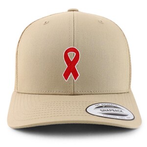 Peut inclure: Casquette de camionneur beige avec un ruban rouge brodé sur le devant. La casquette a une visière incurvée, un dos en filet et une fermeture à pression. Une étiquette blanche et noire est sur le côté inférieur gauche.