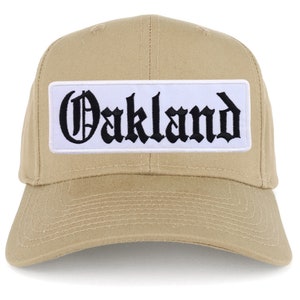 May include: A tan baseball cap with a white patch that says "Oakland" in black gothic lettering.