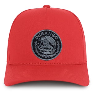 Könnte beinhalten: Rote Baseballkappe mit einem kreisförmigen Aufnäher mit dem Wort "DURANGO" und einem Adleremblem. Die Kappe hat einen gebogenen Schirm und eine strukturierte Krone. Der Aufnäher ist in Grau- und Schwarztönen gehalten.