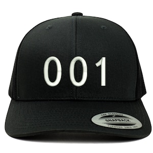 Könnte beinhalten: Schwarze Trucker-Kappe mit weißem Netzrücken. Die Vorderseite der Kappe trägt die Nummer "001" in Weiß.