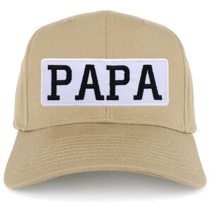 Puede incluir: Una gorra de béisbol de color beige con un parche blanco que dice "PAPA" en letras negras.