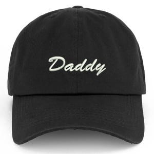 May include: Black baseball cap with the word "Daddy" embroidered in white script across the front. The cap has a curved brim and an adjustable strap at the back. A casual accessory.