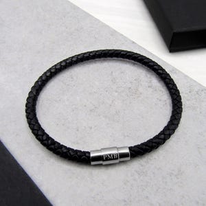 May include: A black leather bracelet with a silver magnetic clasp engraved with the initials "PMB".