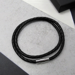 May include: A black leather bracelet with a braided design and a silver magnetic clasp.