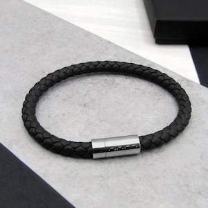May include: A black leather bracelet with a braided design and a silver magnetic clasp.
