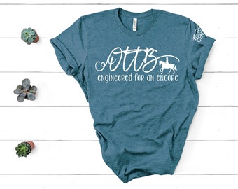 May include: A teal blue t-shirt with white text that reads "OTTB Engineered for an Encore" and a silhouette of a person riding a horse.