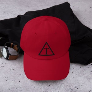 May include: A red baseball cap with a black triangle and the letter "T" embroidered on the front.