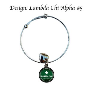 Puede incluir: Un brazalete extensible de plata con un dije verde que dice "Lambda Chi Fraternity" con una cruz blanca.
