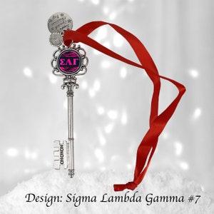 May include: A silver key-shaped ornament with a pink and black circle featuring the letters "ΣΛΓ" and the words "HOHOHO" on the side. The ornament is attached to a red ribbon.