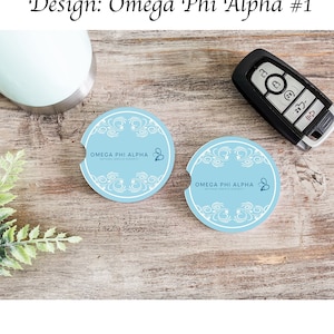 Könnte beinhalten: Zwei runde Untersetzer in Blau und Weiß mit dem Text "OMEGA PHI ALPHA NATIONAL SERVICE SORORITY". Die Untersetzer liegen auf einer Holzoberfläche.