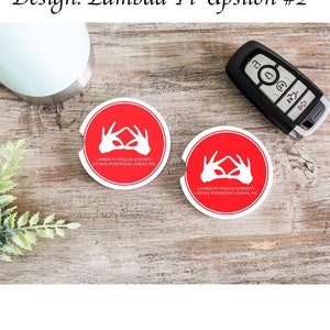 Op de afbeelding: Twee ronde rode drinkonderzetters met witte contouren. Elke onderzetter heeft een wit hands symbool met de tekst "Lambda Pi Upsilon Sorority, Latinas Poderosas Unidas, Inc."
