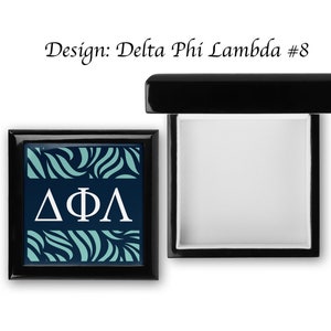 May include: Black wooden box with a teal and navy blue patterned design and the letters "ΔΦΛ" in white. The box is open and the inside is white.