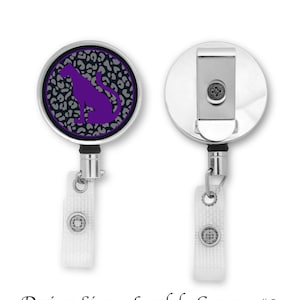 Könnte beinhalten: Ein silberner ausziehbarer Ausweishalter mit einem runden, schwarz-weißen Leopardenmuster, das eine violette Silhouette eines Panthers zeigt. Der Text "Sigma Lambda Gamma #2" ist unter dem Bild gedruckt.