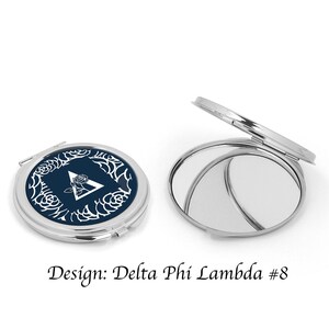 May include: A silver compact mirror with a navy blue lid featuring a white rose and a white triangle with the letter A inside. The text "Design: Delta Phi Lambda #8" is below the mirror.