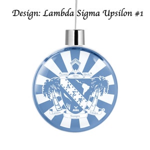 Op de afbeelding: Een blauwe en witte kerstbal met een wapenschild met de letters Lambda Sigma Upsilon, palmbomen en de woorden "Latinos Unidos Siempre".