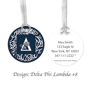 May include: A navy blue luggage tag with a white floral design and the letter A in the center. The back of the tag has the text "Alex Smith, 123 Eagle St, New York, NY 10001, 347-111-2222 *example name and address". The tag is labeled "Design: Delta Phi Lambda #8".