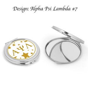 May include: A silver compact mirror with a white background and gold lettering that reads "ΑΨΛ" surrounded by gold stars. The mirror is closed.