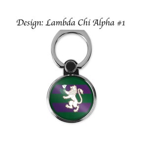 May include: A silver phone ring holder with a round, green and purple design featuring a white lion holding a white flower. The design says "Lambda Chi Alpha #1".