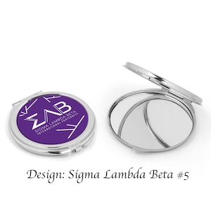 May include: A compact mirror with a purple lid featuring the Sigma Lambda Beta sorority logo and the text "Sigma Lambda Beta International Fraternity".