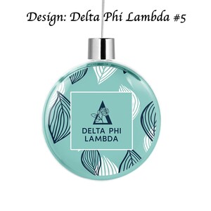 Könnte beinhalten: Ein türkisfarbener Weihnachtsbaumschmuck mit einem weißen und schwarzen Blattmotiv. Der Schmuck zeigt ein weißes Quadrat mit einem schwarzen Dreieck und einer Rose darin. Der Text "DELTA PHI LAMBDA" ist in Schwarz innerhalb des Quadrats gedruckt.