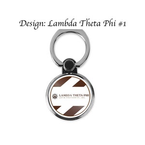 May include: A silver phone ring holder with a white and brown circle attached. The circle has a logo that says "Lambda Theta Phi Latin Fraternity, Inc."