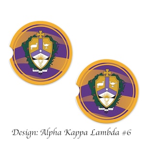 May include: Two round, yellow and purple car coasters with a crest featuring a white star, a lamb, a bird, and a sunburst. The crest is surrounded by green leaves and a purple shield. The text "Veritas Vox Alma" is written in a circle around the crest.