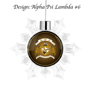 Könnte beinhalten: Ein schneeflockenförmiger Weihnachtsbaumschmuck mit einem goldenen und braunen runden Design mit den griechischen Buchstaben "ΨA" und dem Text "Est. 1985" und "We Shall Seek The" in einem Banner.