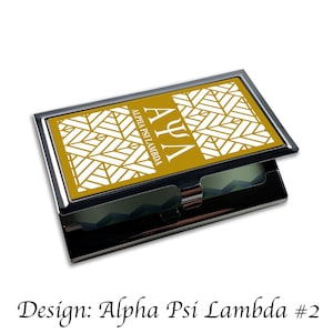 Op de afbeelding: Een gouden en witte visitekaartjeshouder met een geometrisch patroon en de tekst "ΑΨΛ Alpha Psi Lambda" aan de voorkant.