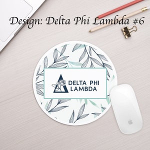 May include: A white round mouse pad with a blue and green floral design. The center of the mouse pad features a white rectangle with the text "DELTA PHI LAMBDA" and a blue triangle with a rose inside.