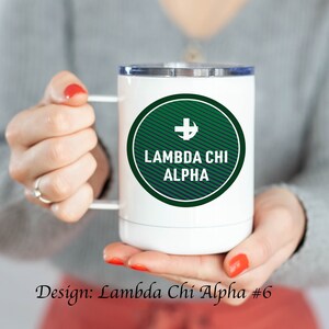 May include: White travel mug with a green and navy blue circle design. The circle has a white cross with an anchor inside and the text "Lambda Chi Alpha".