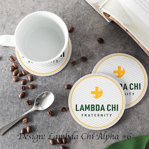 May include: Two round coasters with a white background and a yellow and gray striped pattern. The coasters feature a green and yellow logo with a cross and a crescent moon. The text "Lambda Chi Fraternity" is printed on the coasters.