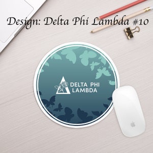 Może przedstawiać: Okrągła podkładka pod mysz z niebiesko-zielonym gradientem tła. Projekt zawiera biały tr&oacute;jkąt z r&oacute;żą w środku i tekstem "DELTA PHI LAMBDA". Tło jest ozdobione białymi motylami.