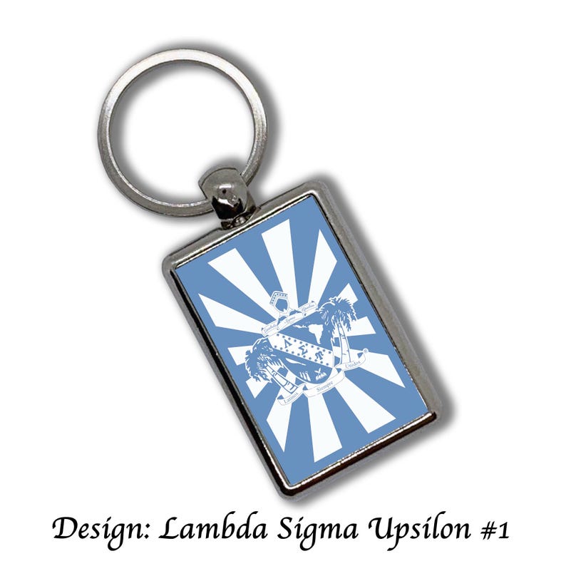 May include: Rectangular silver keychain with a light blue background featuring a white design of a crest, palm trees, and radiating lines. The text "Design: Lambda Sigma Upsilon #1" is at the bottom.