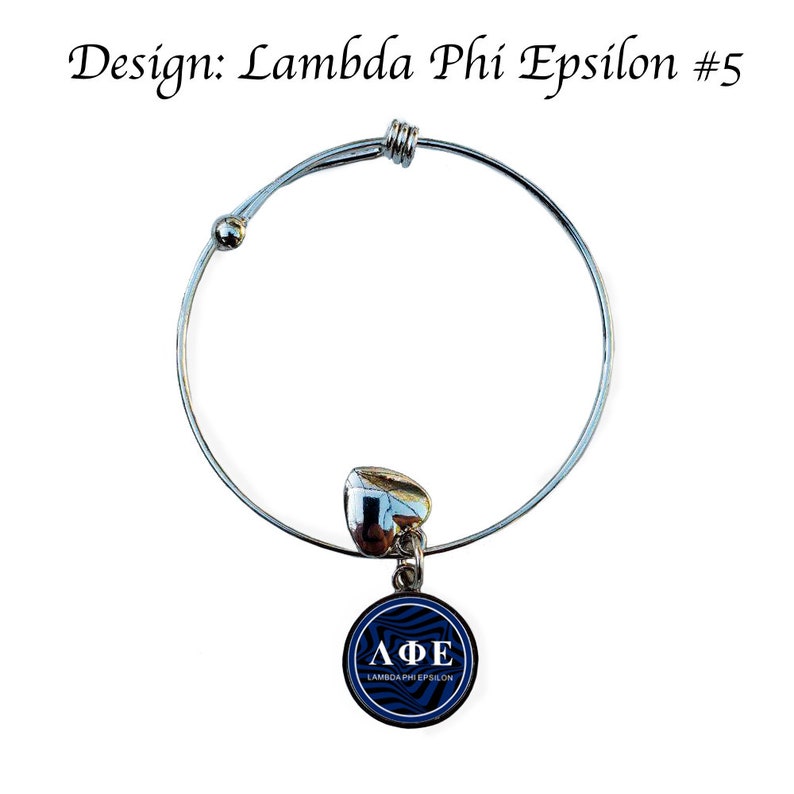 May include: A silver expandable bracelet with a heart charm and a round charm featuring a blue and white swirl design. The round charm displays the letters "&Lambda;&Phi;&Epsilon;" and the words "Lambda Phi Epsilon".