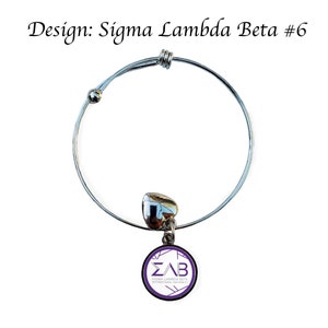 K&ouml;nnte beinhalten: Ein silbernes, ausziehbares Armband mit einem Herz-Anh&auml;nger und einem runden Anh&auml;nger mit den Buchstaben "&Sigma;&Lambda;&Beta;" und dem Text "Sigma Lambda Beta International Fraternity".