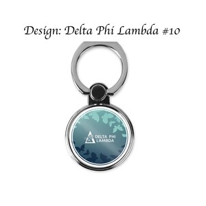 Op de afbeelding: Een zilveren telefoonringhouder met een rond, blauwgroen en blauw ontwerp met vlinders en de tekst "DELTA PHI LAMBDA". De tekst "Design: Delta Phi Lambda #10" staat boven de ringhouder.
