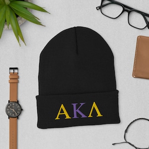 May include: Black knit beanie with a gold and purple embroidered "AKA" logo.