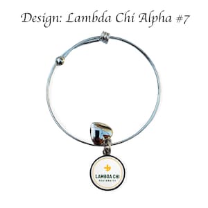 Puede incluir: Un brazalete extensible de plata con un dije en forma de coraz&oacute;n y un dije redondo con el texto "Lambda Chi Fraternity" en verde y dorado sobre un fondo blanco.
