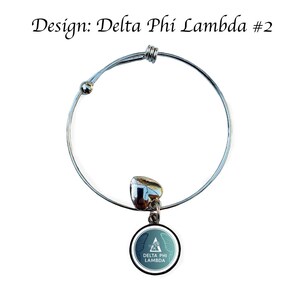 K&ouml;nnte beinhalten: Silbernes, ausziehbares Armband mit einem Anh&auml;nger mit einem blaugr&uuml;nen und wei&szlig;en Design mit dem Text "Delta Phi Lambda".