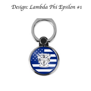 Może przedstawiać: Srebrny uchwyt na pierścień do telefonu z wzorem amerykańskiej flagi w kolorze niebieskim i białym, przedstawiający herb z tekstem "HITS MONKEY - PHI - ANTIPODES - EYNAL".