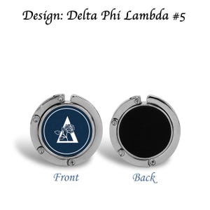May include: A silver-toned purse hook with a navy blue and white design on the front and a black surface on the back. The front features a white triangle and rose design. Text at the top reads "Design: Delta Phi Lambda #5".